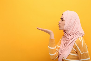 Muslim woman in hijab blowing kiss on orange background, space for text