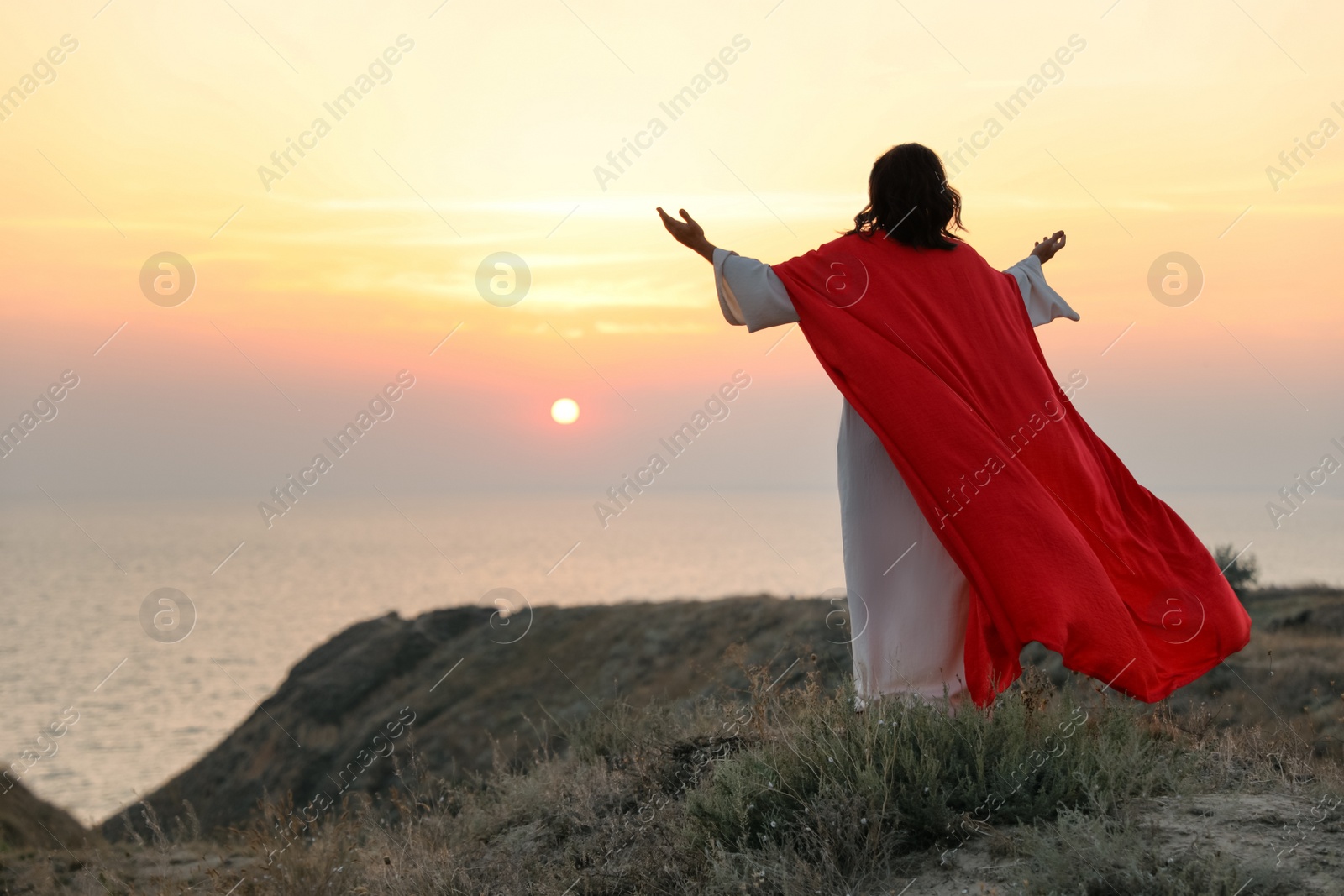 Photo of Jesus Christ raising hands on hills at sunset, back view. Space for text