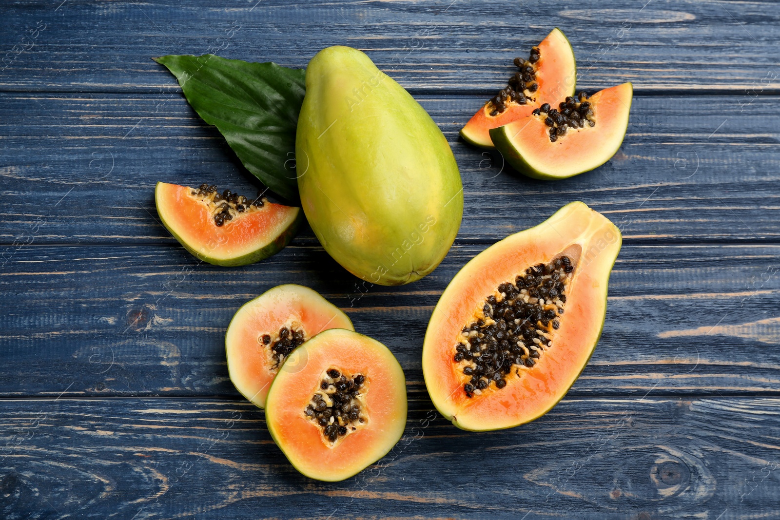 Photo of Fresh ripe papaya fruits with green leaf on blue wooden table, flat lay