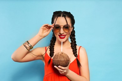 Photo of Young woman with fresh coconut on light blue background. Exotic fruit