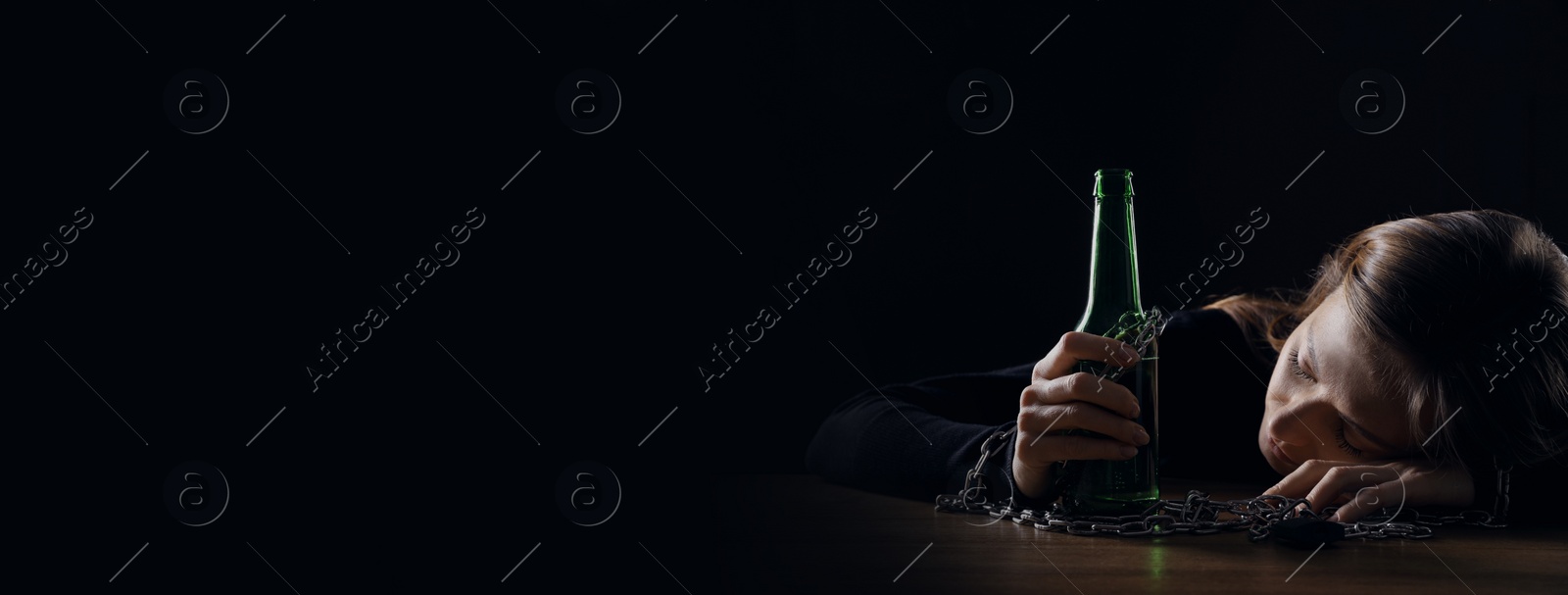 Image of Suffering from hangover. Woman chained with bottle of beer sleeping at table against black background, space for text. Banner design