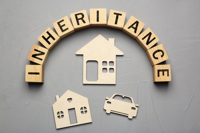 Photo of Word Inheritance made with wooden cubes, car and houses models on grey background, flat lay
