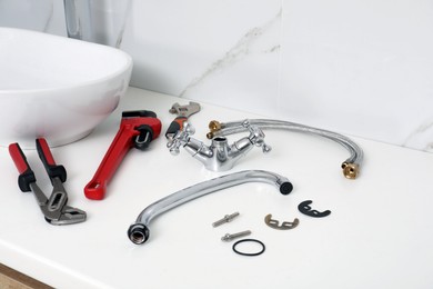 Photo of Parts of water tap and wrenches on white countertop in bathroom