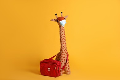 Photo of Toy giraffe with face mask and first aid bag on yellow background. Pediatrician practice