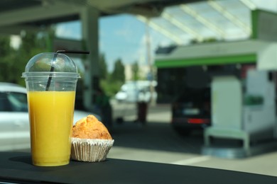 Photo of Plastic cup of juice and muffin on car dashboard at gas station. Space for text