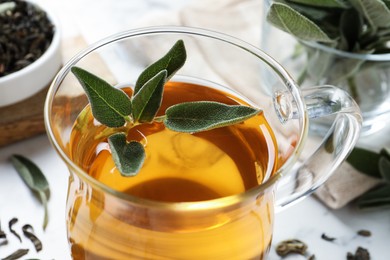 Cup of aromatic sage tea with fresh leaves on table, closeup