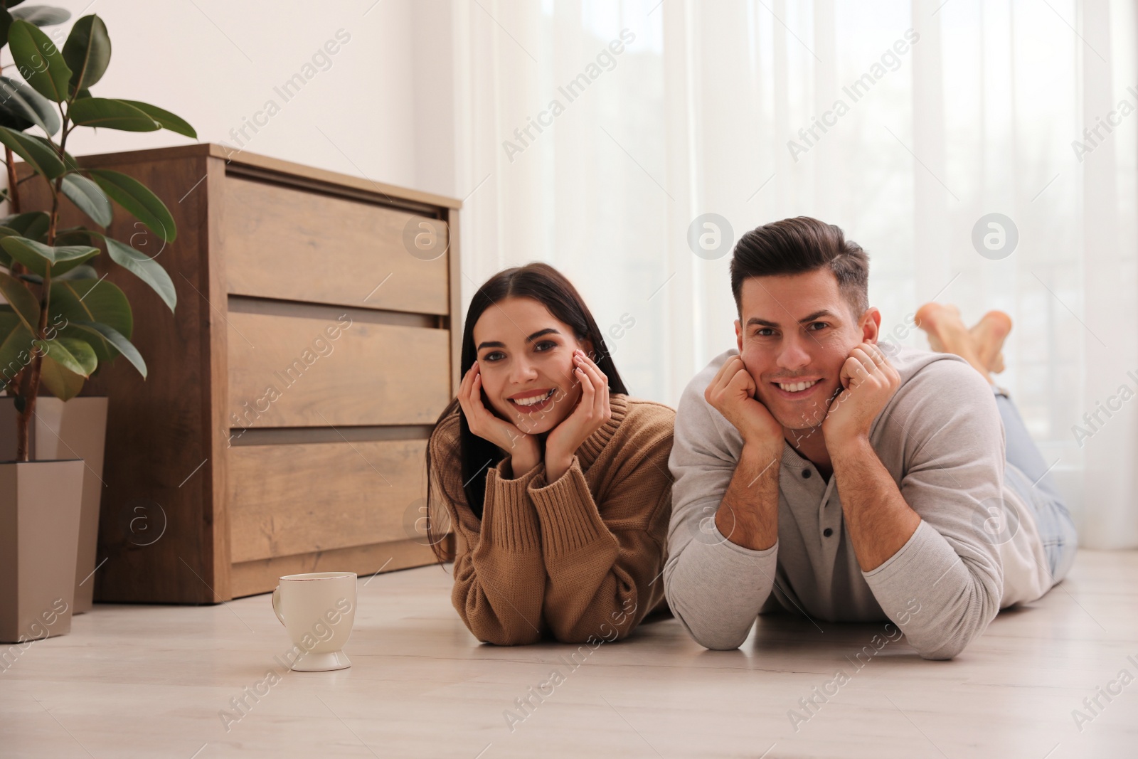 Photo of Happy couple lying on warm floor at home. Heating system