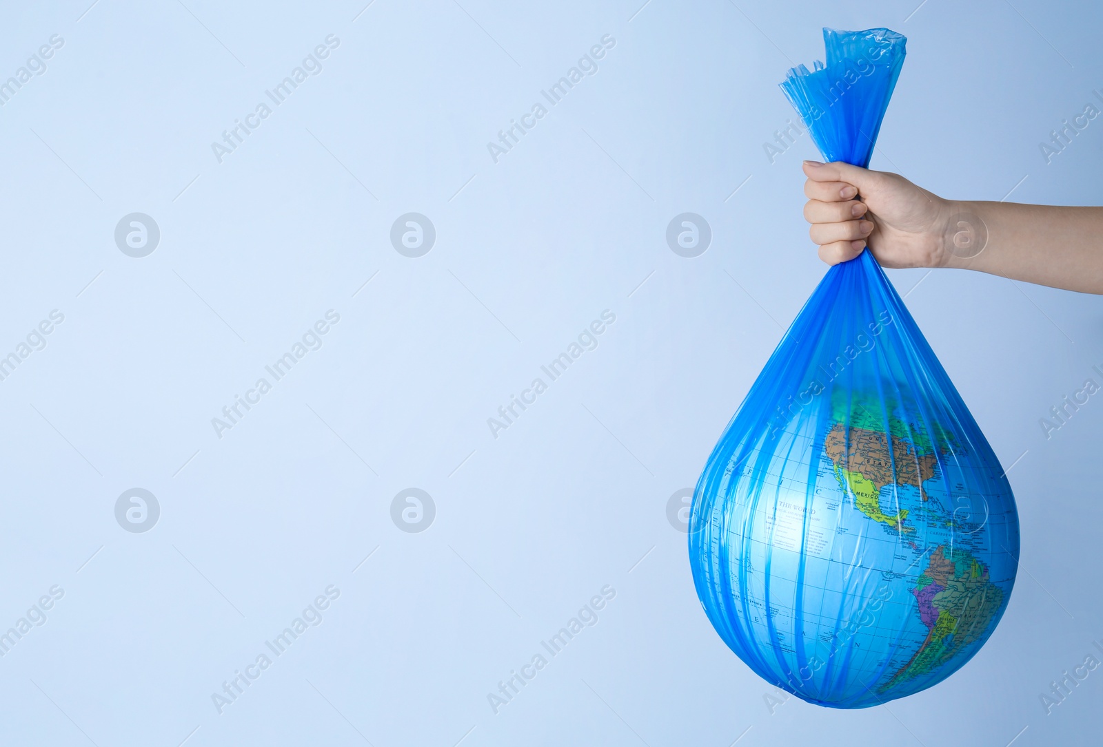Photo of Woman holding plastic bag with globe and space for text on light background, closeup. Environmental conservation