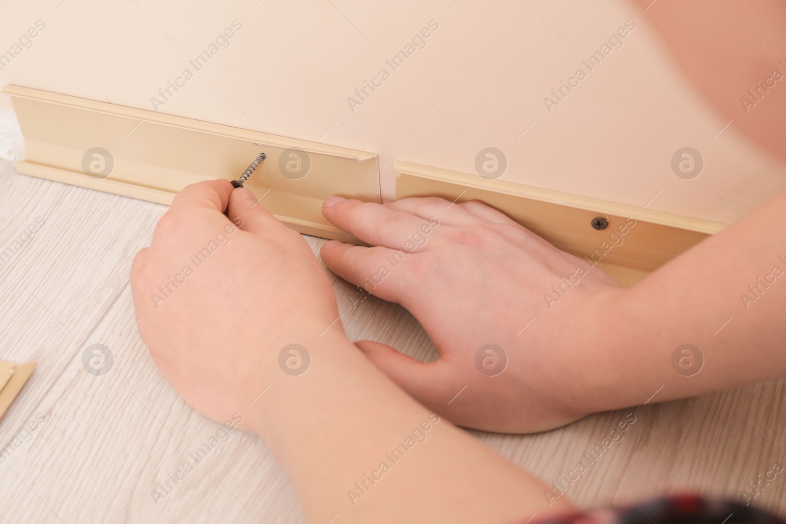 Photo of Man installing plinth on laminated floor in room, closeup