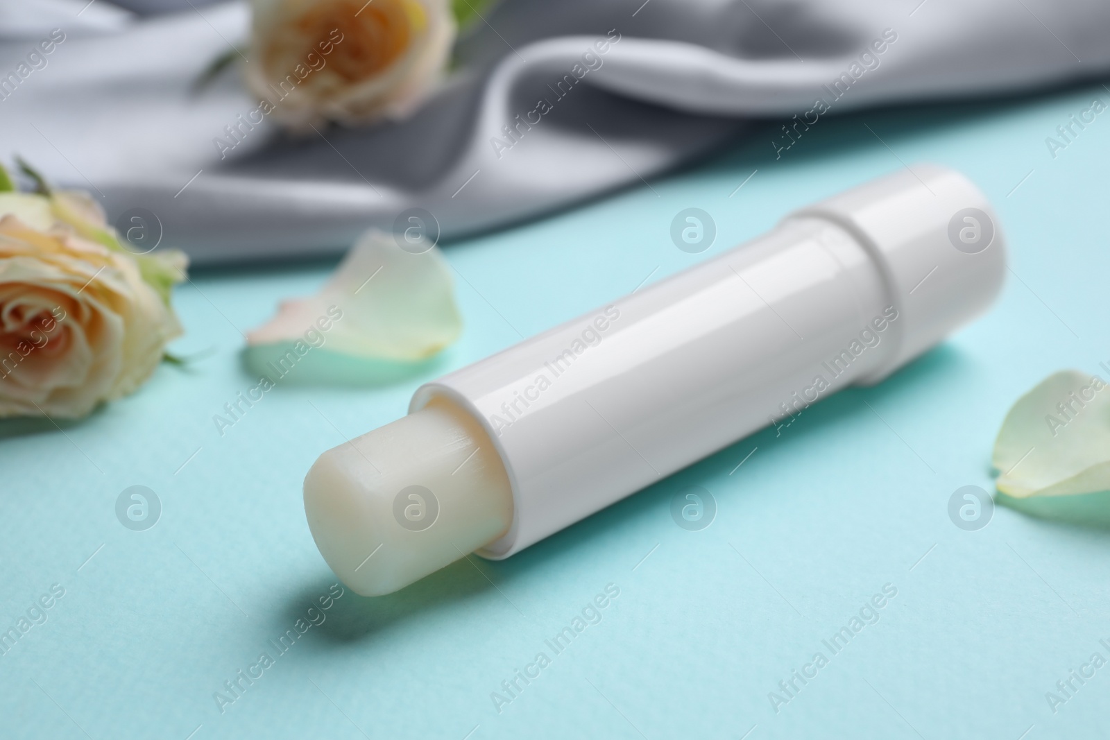 Photo of Hygienic lipstick and rose flower on turquoise background, closeup