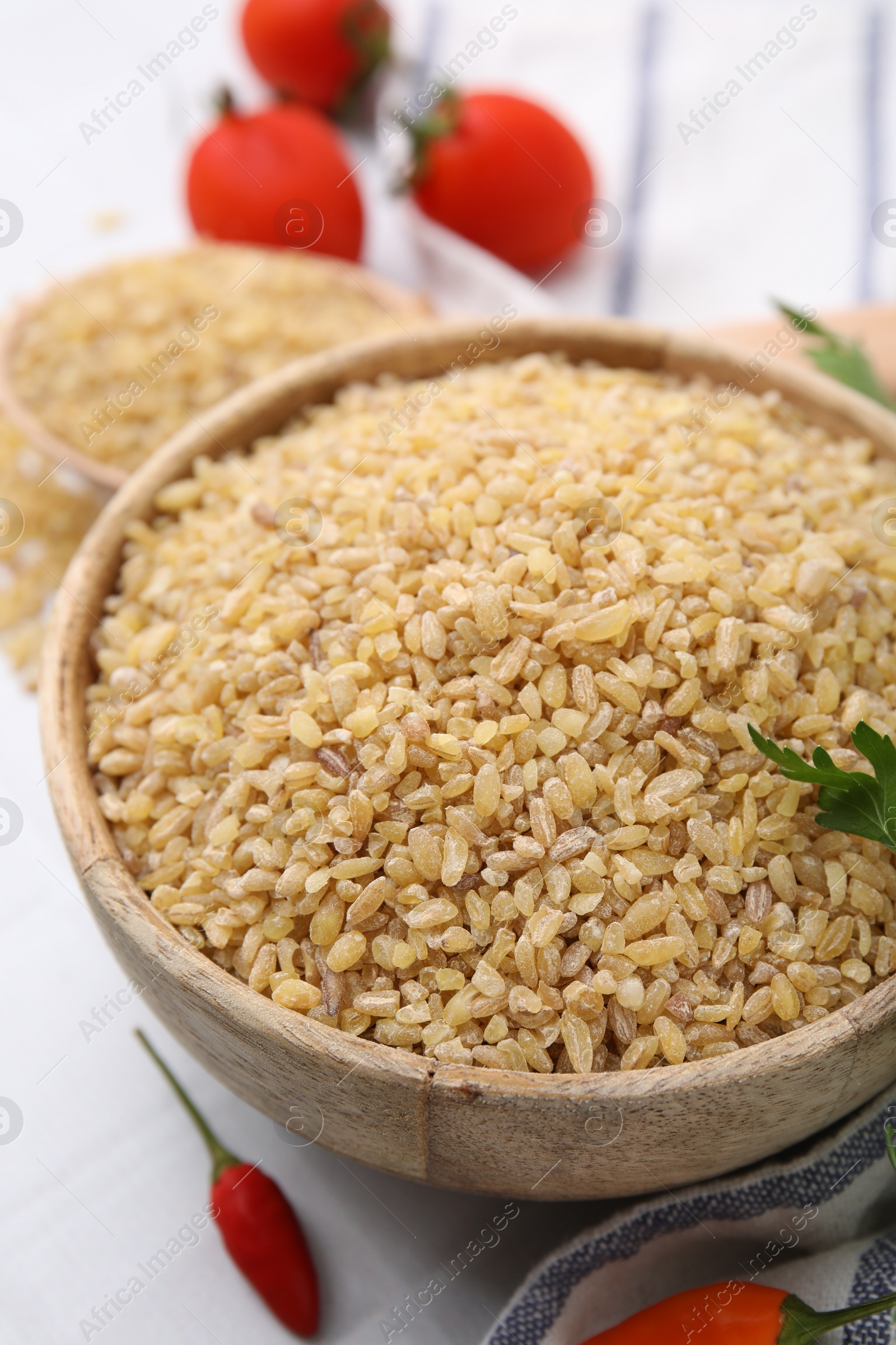 Photo of Raw bulgur in bowl and peppers on table, closeup