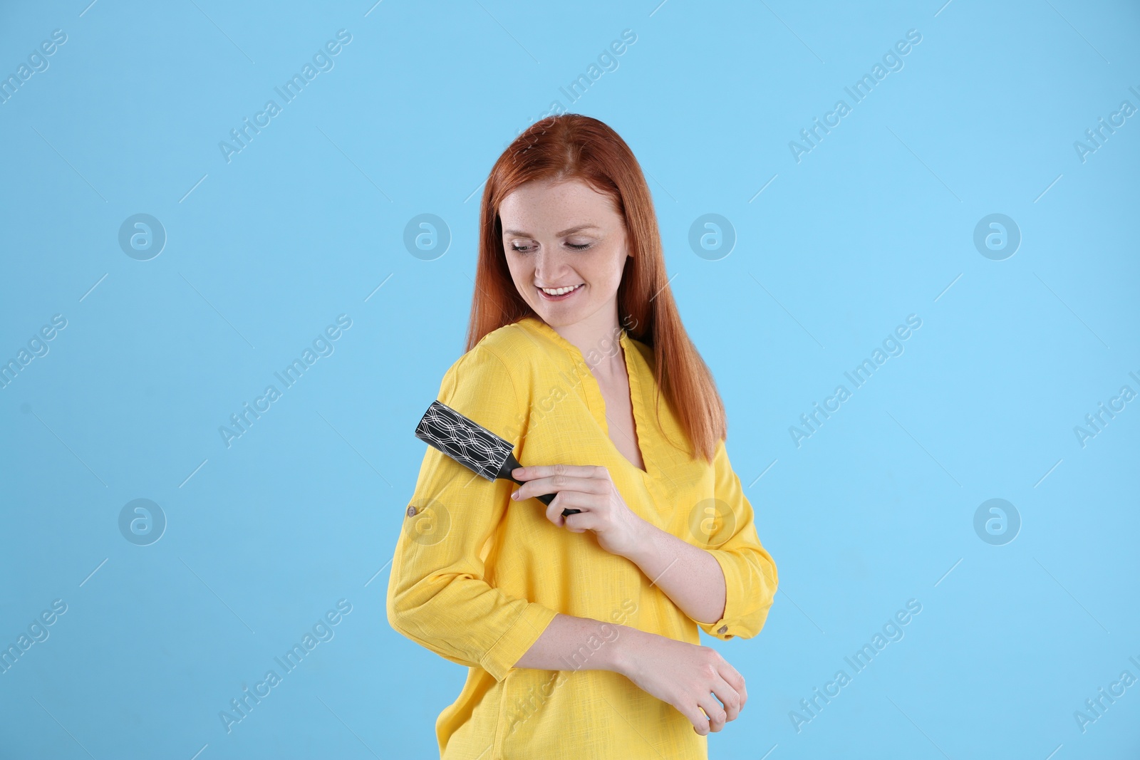 Photo of Young woman cleaning clothes with lint roller on light blue background