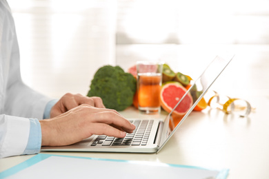 Photo of Nutritionist working with laptop at desk in office, closeup