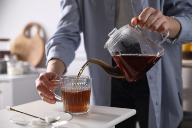 Photo of Woman pouring hot tea into cup at white table, closeup