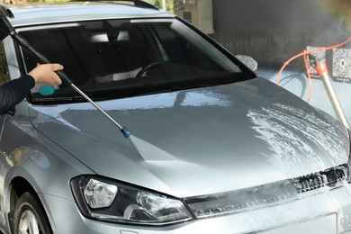 Man washing auto with high pressure water jet at outdoor car wash, closeup