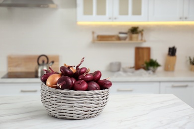 Photo of Basket with fresh onions on white marble table in modern kitchen. Space for text