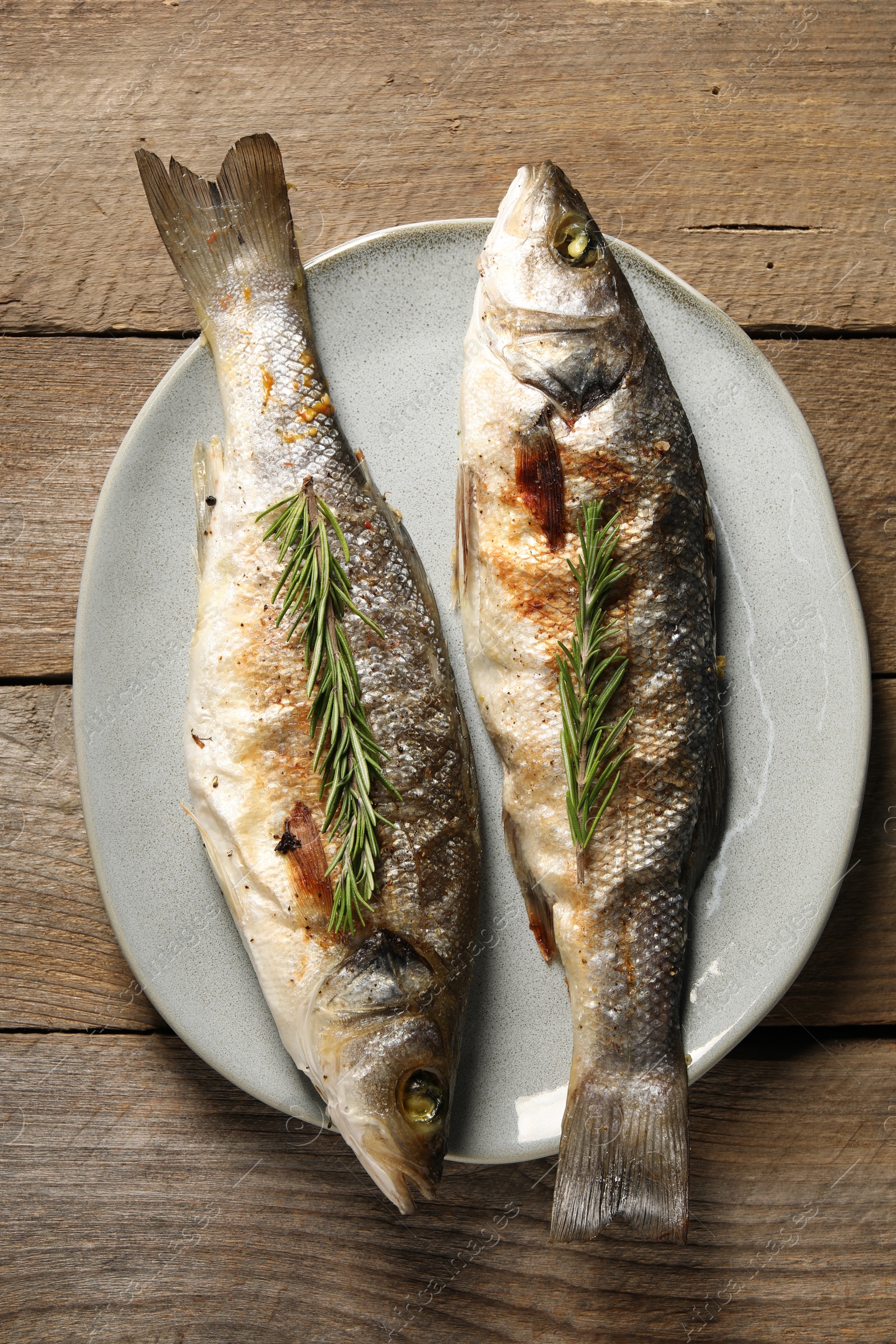 Photo of Delicious baked fish and rosemary on wooden table, top view