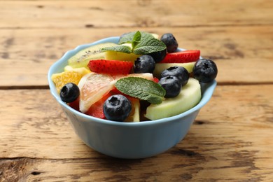 Photo of Tasty fruit salad in bowl on wooden table, closeup