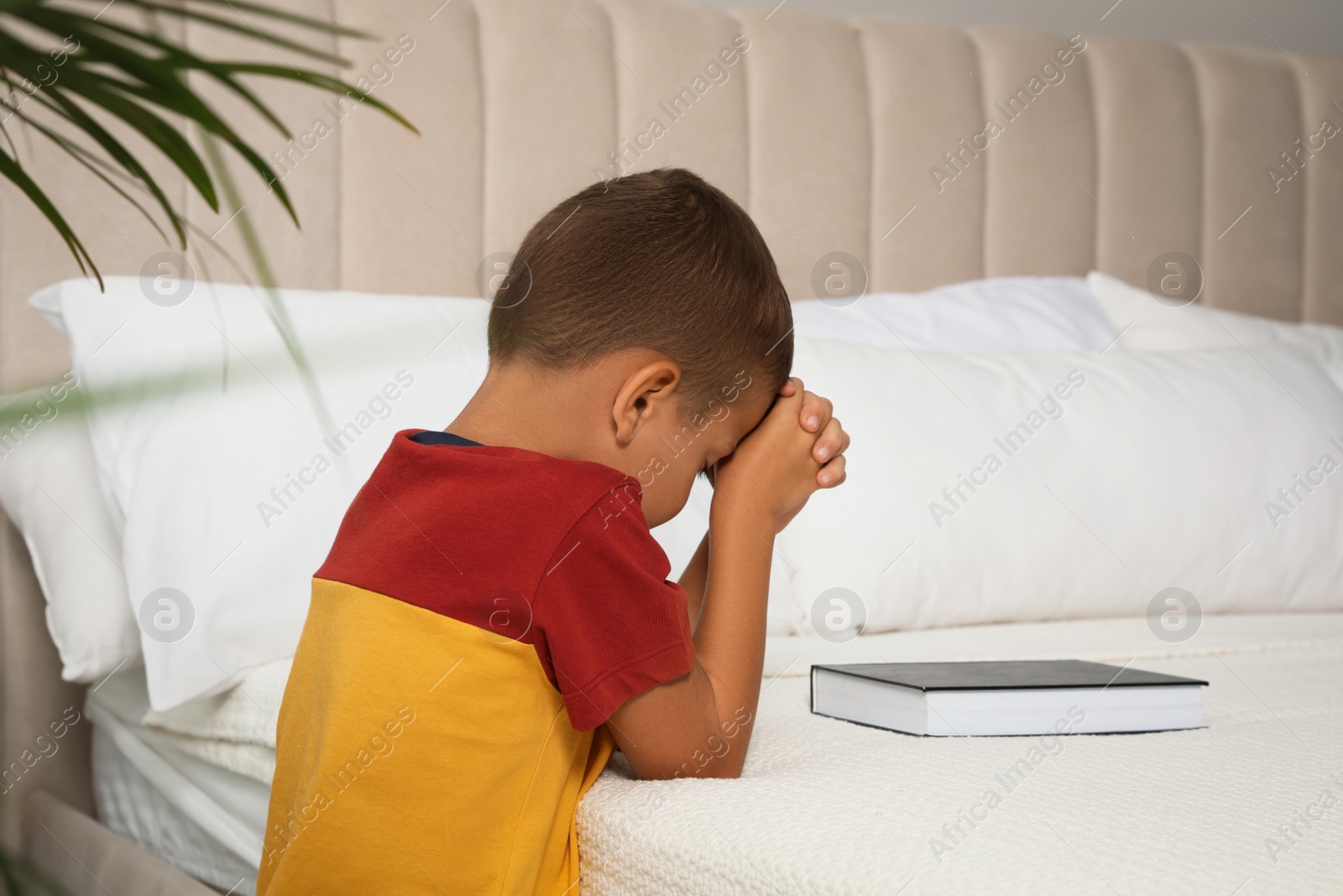 Photo of Cute little boy with hands clasped together saying bedtime prayer over Bible at home. Space for text