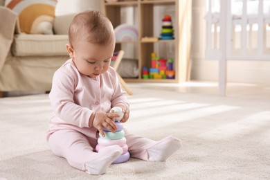 Cute baby girl playing with toy pyramid on floor at home