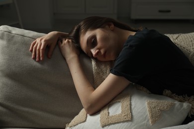 Photo of Sad young woman lying on sofa at home