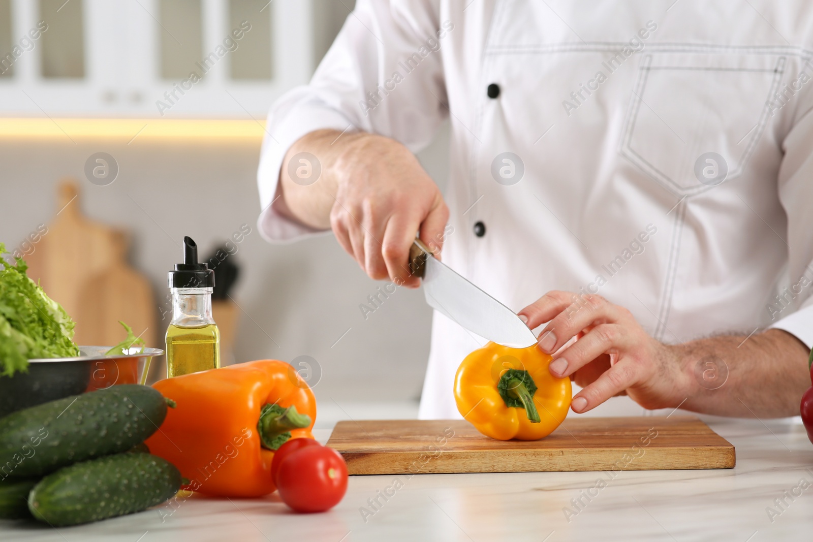 Photo of Chef cutting bell pepper at marble table in kitchen, closeup