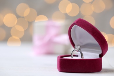 Photo of Box with ring on table against blurred lights. Space for text