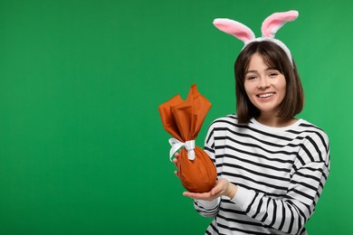 Easter celebration. Happy woman with bunny ears and wrapped egg on green background, space for text