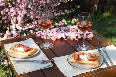 Photo of Delicious Belgian waffles with fresh strawberries and wine served on table in spring garden