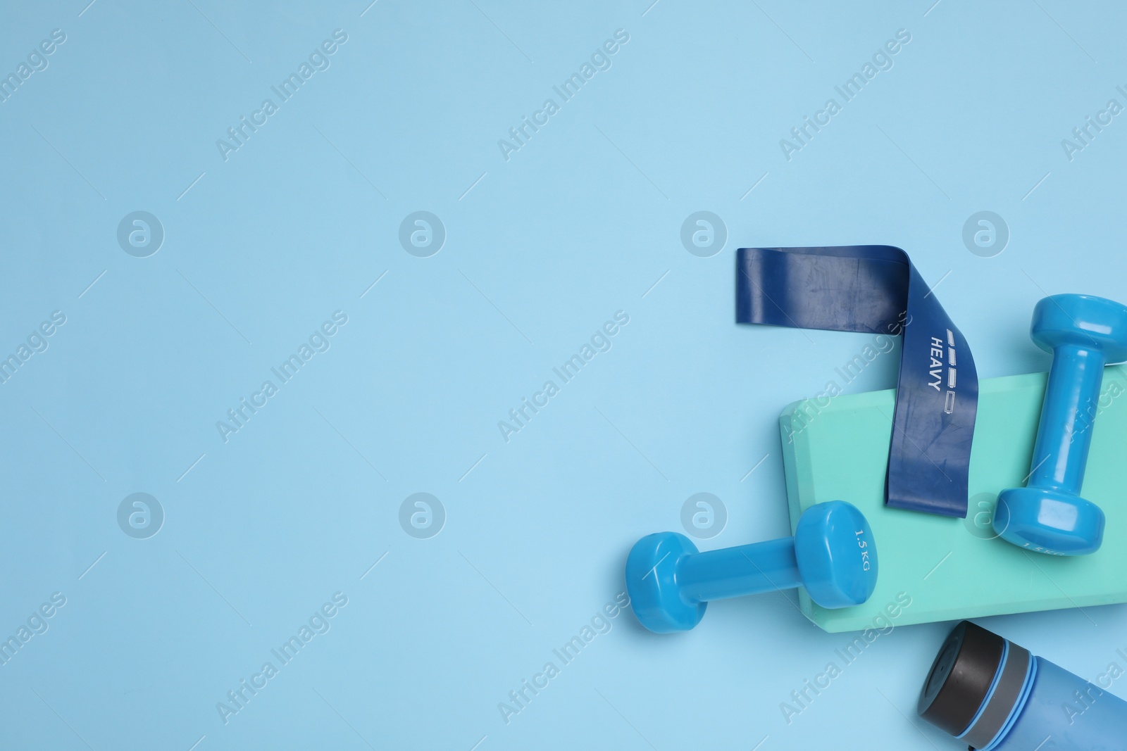 Photo of Two dumbbells, yoga block, fitness elastic band and bottle on light blue background, flat lay. Space for text