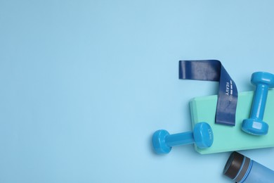 Photo of Two dumbbells, yoga block, fitness elastic band and bottle on light blue background, flat lay. Space for text