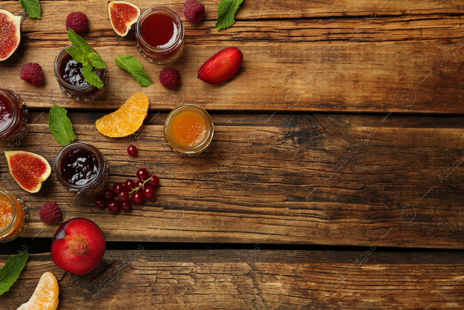 Photo of Jars of different jams and fresh ingredients on wooden table, flat lay. Space for text