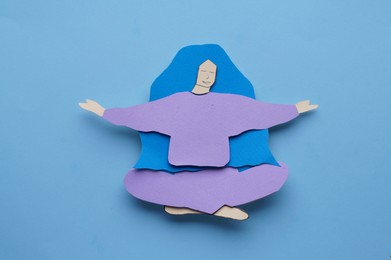 Woman paper figure on light blue background, top view