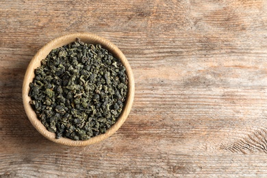 Photo of Bowl of Tie Guan Yin oolong tea leaves on wooden background, top view with space for text