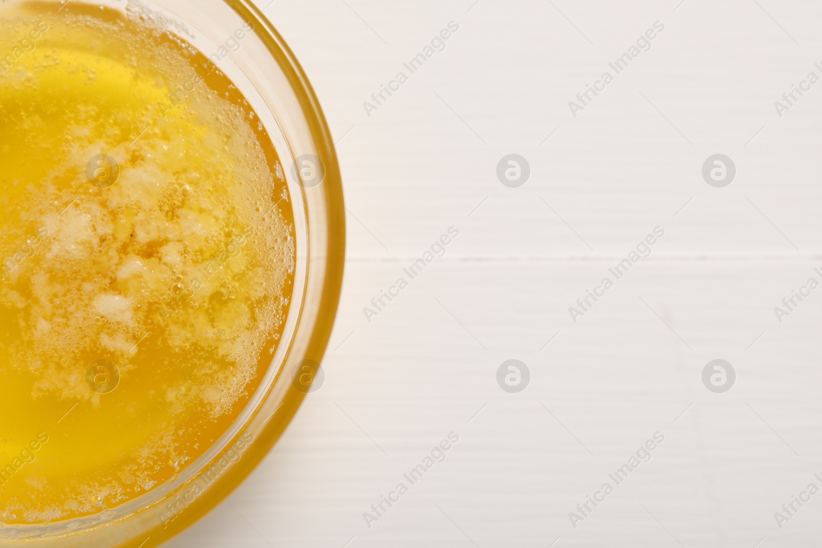 Photo of Melted butter in glass bowl on white wooden table, top view. Space for text