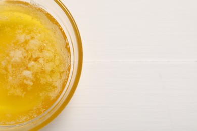 Photo of Melted butter in glass bowl on white wooden table, top view. Space for text