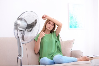 Woman suffering from heat in front of fan at home