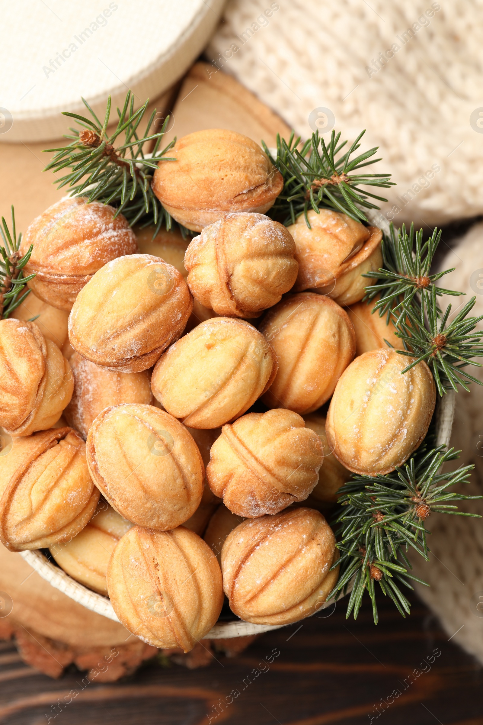 Photo of Bowl of delicious nut shaped cookies and fir tree branches on wooden table, top view