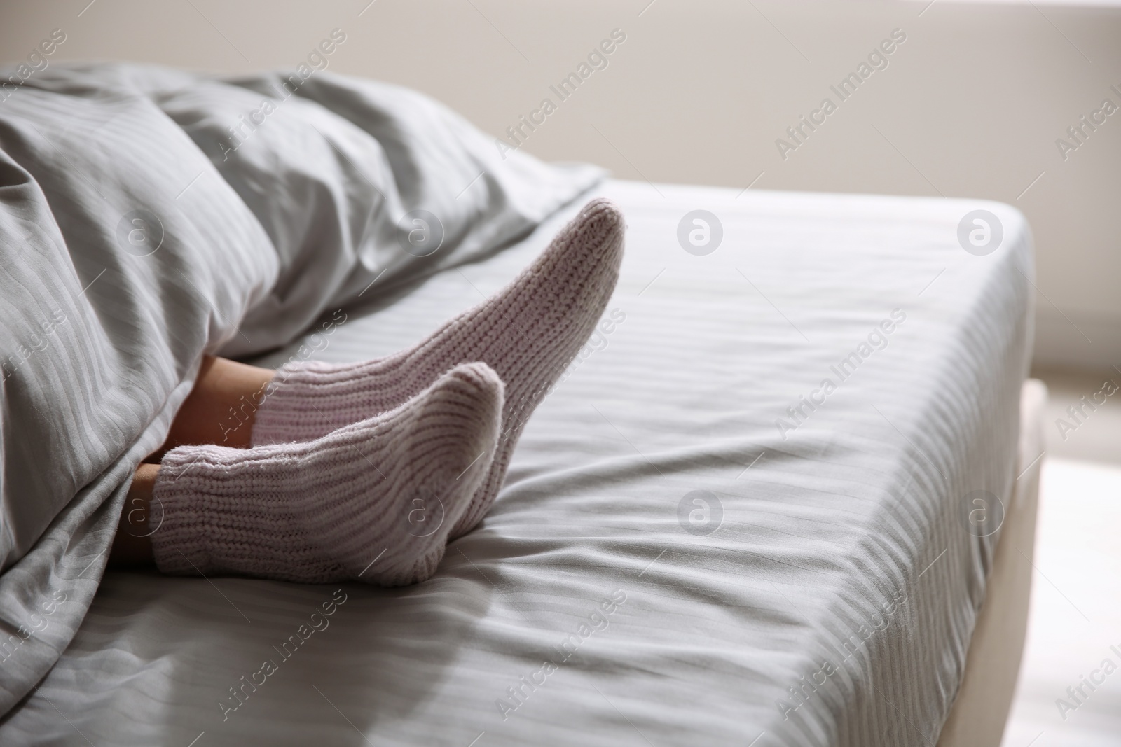 Photo of Woman wearing knitted socks under blanket in bed, closeup. Space for text