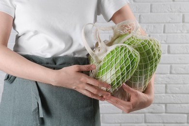 Photo of Woman holding string bag with fresh Chinese cabbages near white brick wall, closeup