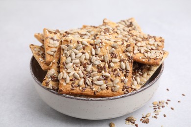 Cereal crackers with flax, sunflower and sesame seeds in bowl on light textured table, closeup