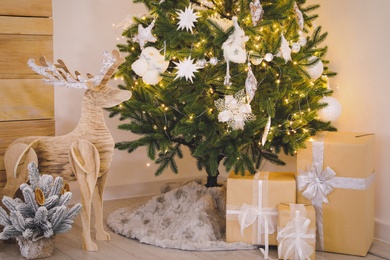 Beautiful decorated Christmas tree with skirt and gifts in room