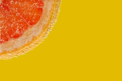 Photo of Slice of grapefruit in sparkling water on yellow background, closeup with space for text. Citrus soda