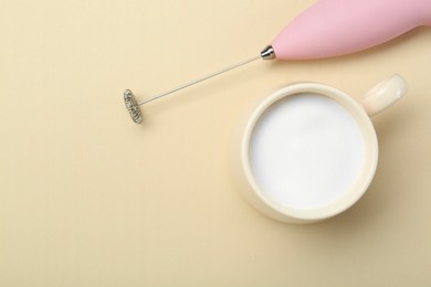 Photo of Mini mixer (milk frother) and cup of whipped milk on beige background, flat lay. Space for text