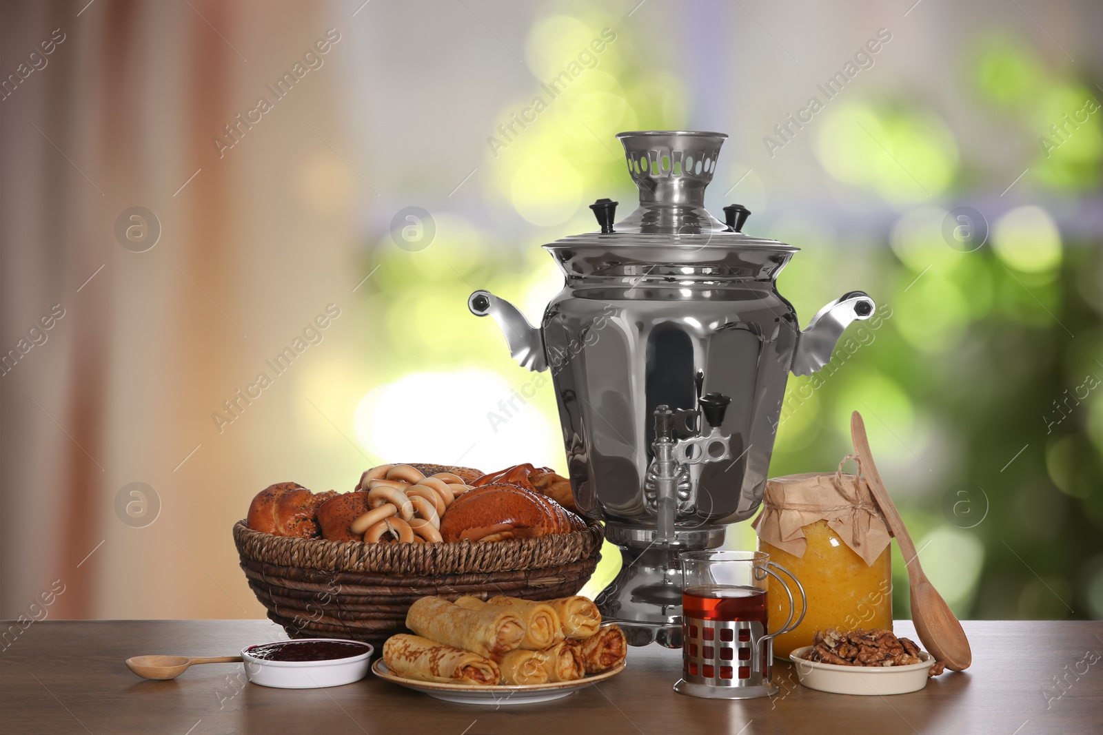 Image of Traditional Russian samovar and treats on wooden table against window in room