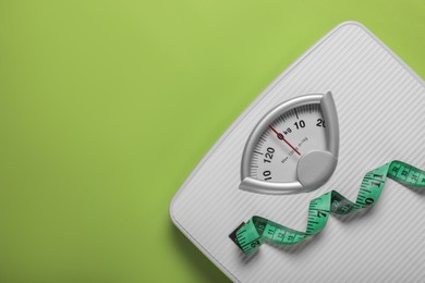 Photo of Weight loss concept. Scales and measuring tape on green background, top view. Space for text