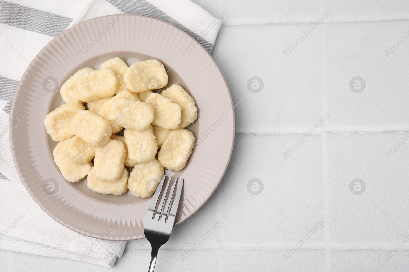 Photo of Plate of tasty lazy dumplings and fork on white tiled table, flat lay. Space for text