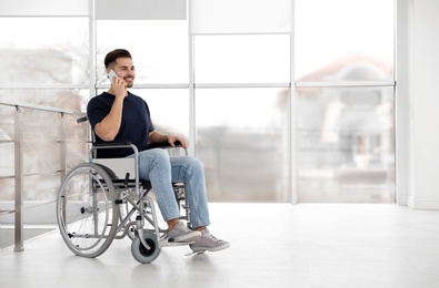 Photo of Young man in wheelchair talking on mobile phone near window indoors