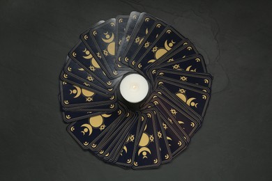 Photo of Tarot cards and burning candle on black table, flat lay. Reverse side