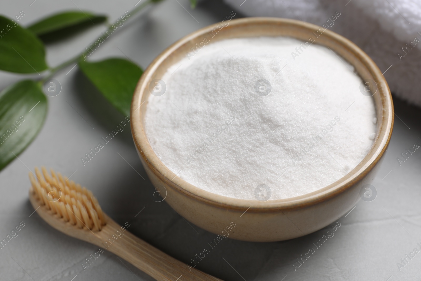 Photo of Bamboo toothbrush, green leaf and bowl of baking soda on grey table, closeup